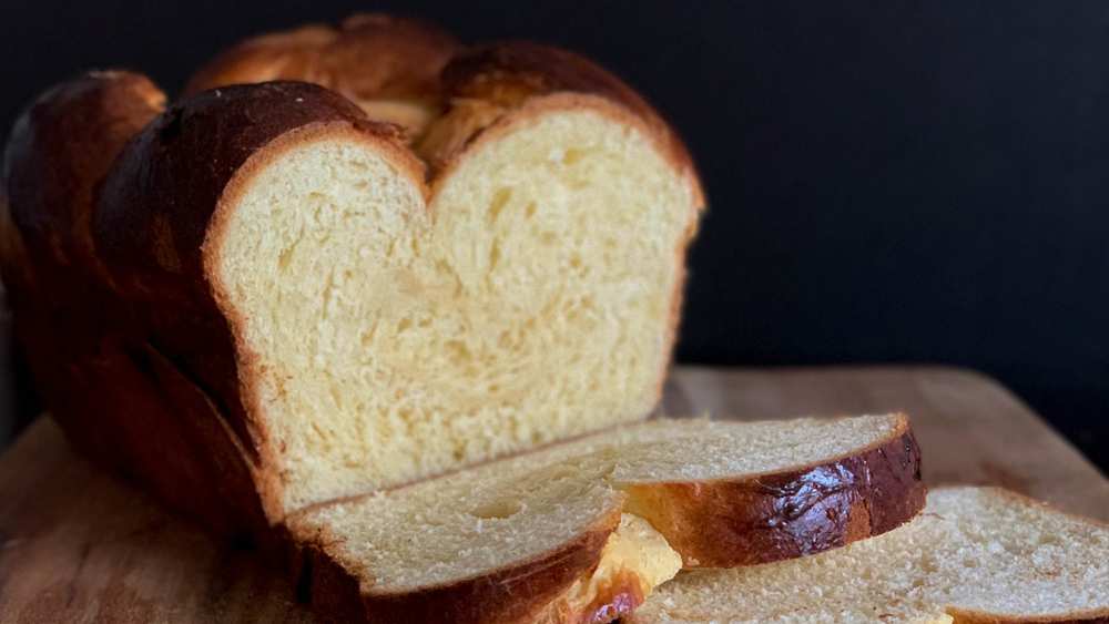 Sliced golden brioche loaf on a wooden board showing a fluffy yellow crumb, a few slices cut, on a dark background