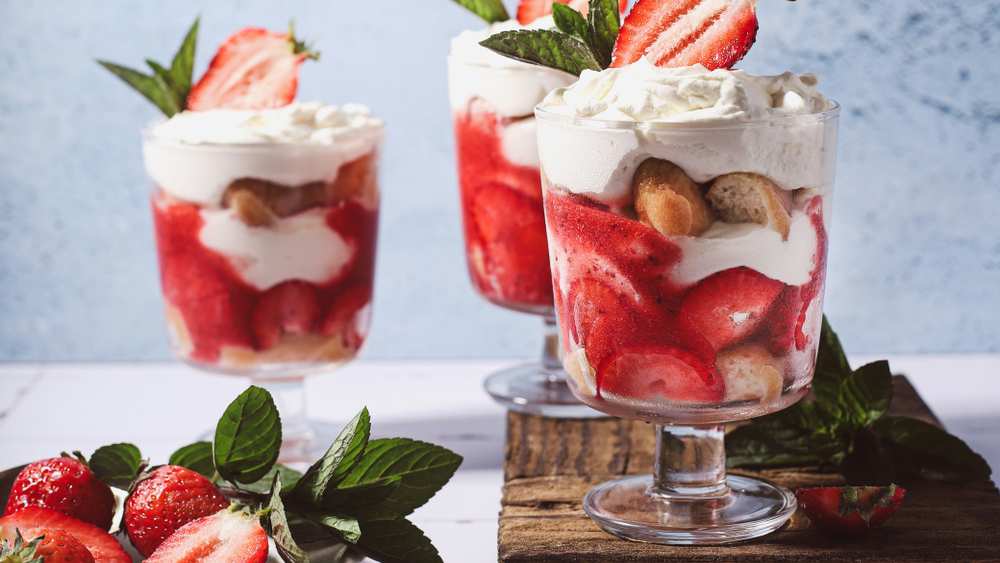 Verrines de tiramisu aux fraises en verres à pied, couches de biscuits, crème et fraises, décorées de chantilly et de menthe