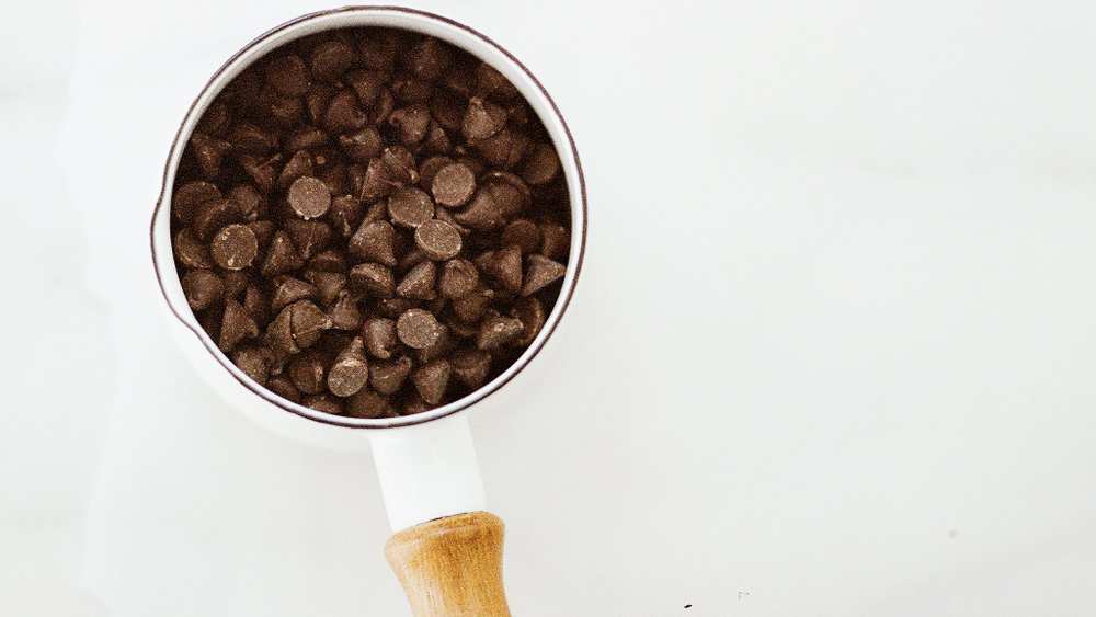 Pépites de chocolat remplissant une petite casserole émaillée blanche à manche en bois, vue de dessus sur marbre