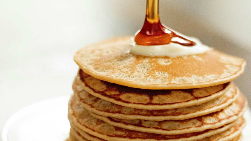 Haute pile de pancakes avec une noix de beurre, du sirop d'érable versé par-dessus, sur une assiette blanche
