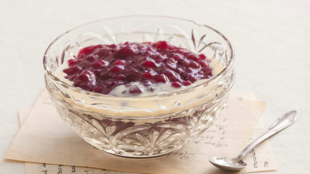 Riz au lait dans un bol en cristal, nappé d'une compotée de fruits rouges, cuillère et fiche recette manuscrite à côté