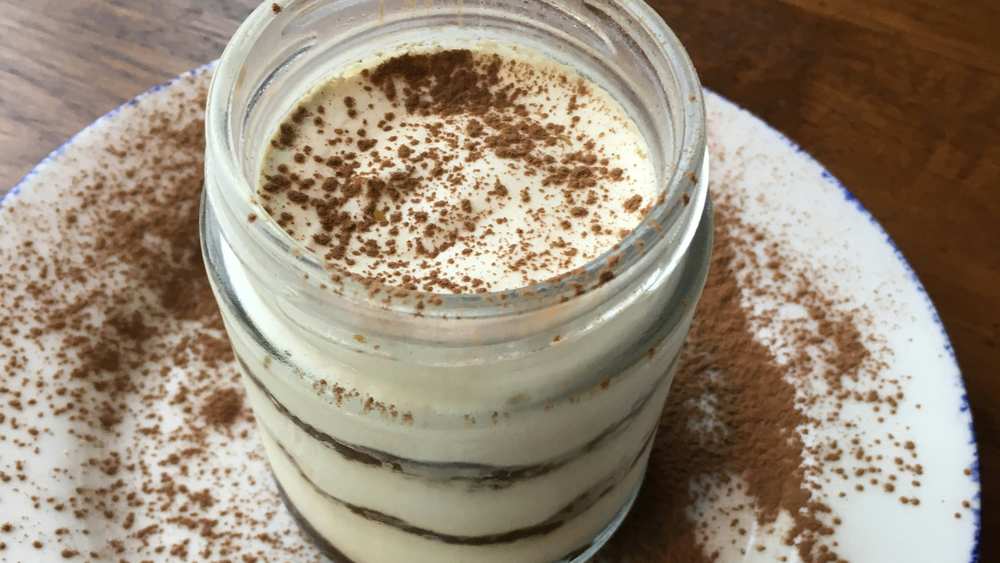 Tiramisu individuel en bocal en verre, couches de crème mascarpone et biscuit, saupoudré de cacao sur une assiette