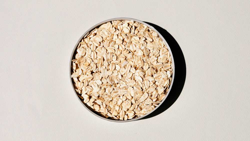 Rolled oats in a round metal tin, seen from above on a pale grey background