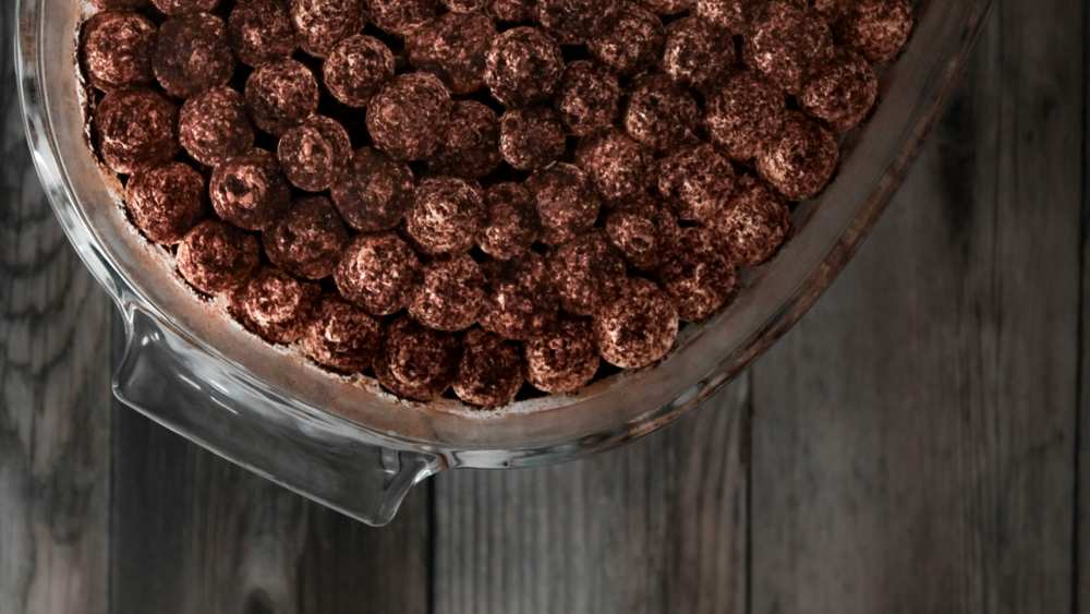 Tiramisu dans un plat en verre, dessus décoré de billes saupoudrées de cacao, sur un fond en bois gris