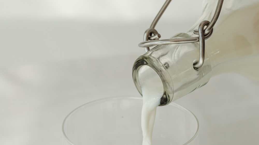 Milk being poured from a swing-top glass bottle into a clear glass, on a white background