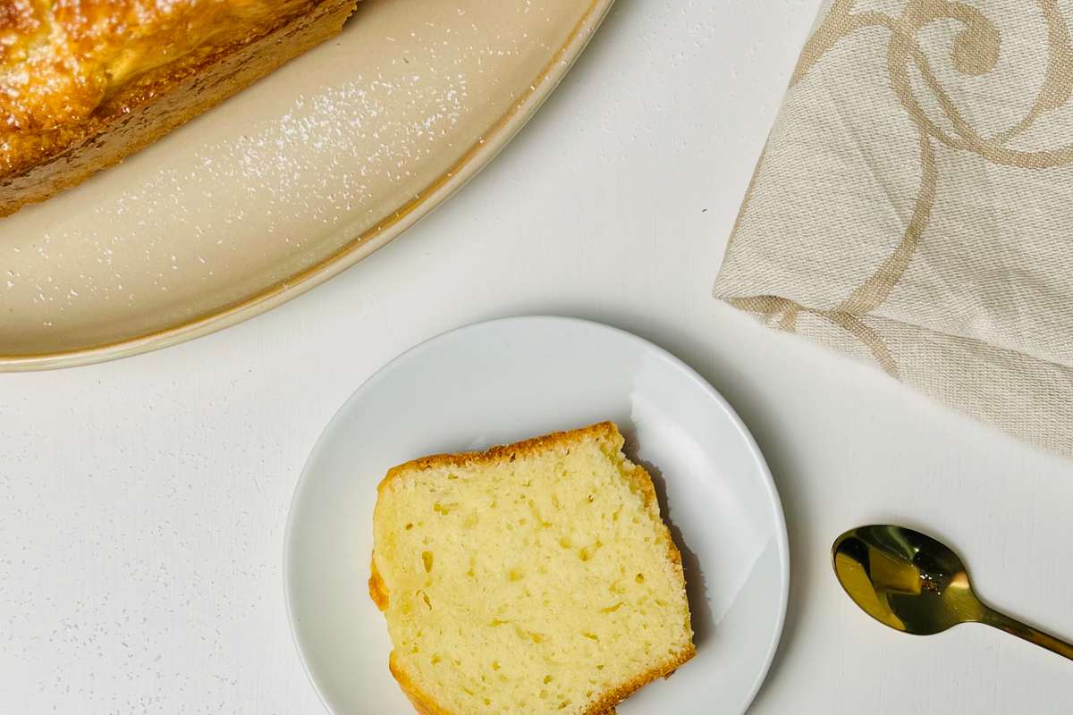 Vue de dessus d'un pain de gâteau, partiellement tranché, et d'une tranche individuelle, sur une surface blanche avec cuillère et serviette.