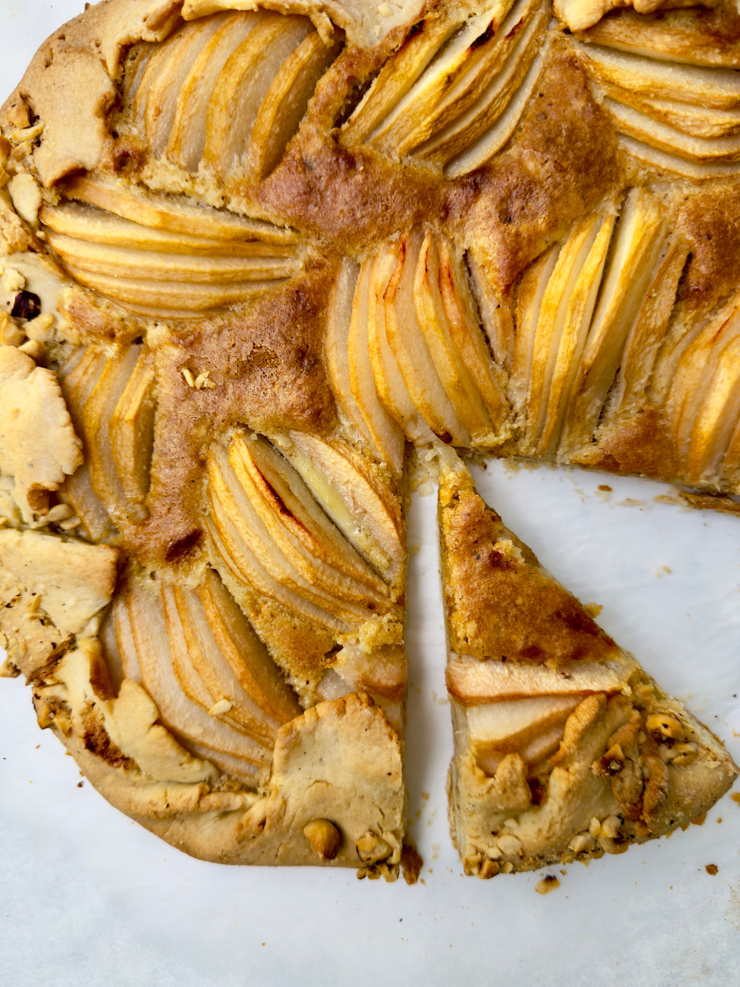Close up of a baked pear tart with a slice cut and placed next to it.