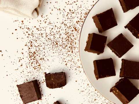 Overhead shot of chocolate fudge squares on a white plate with black and gold rim, scattered cocoa powder, and a napkin.