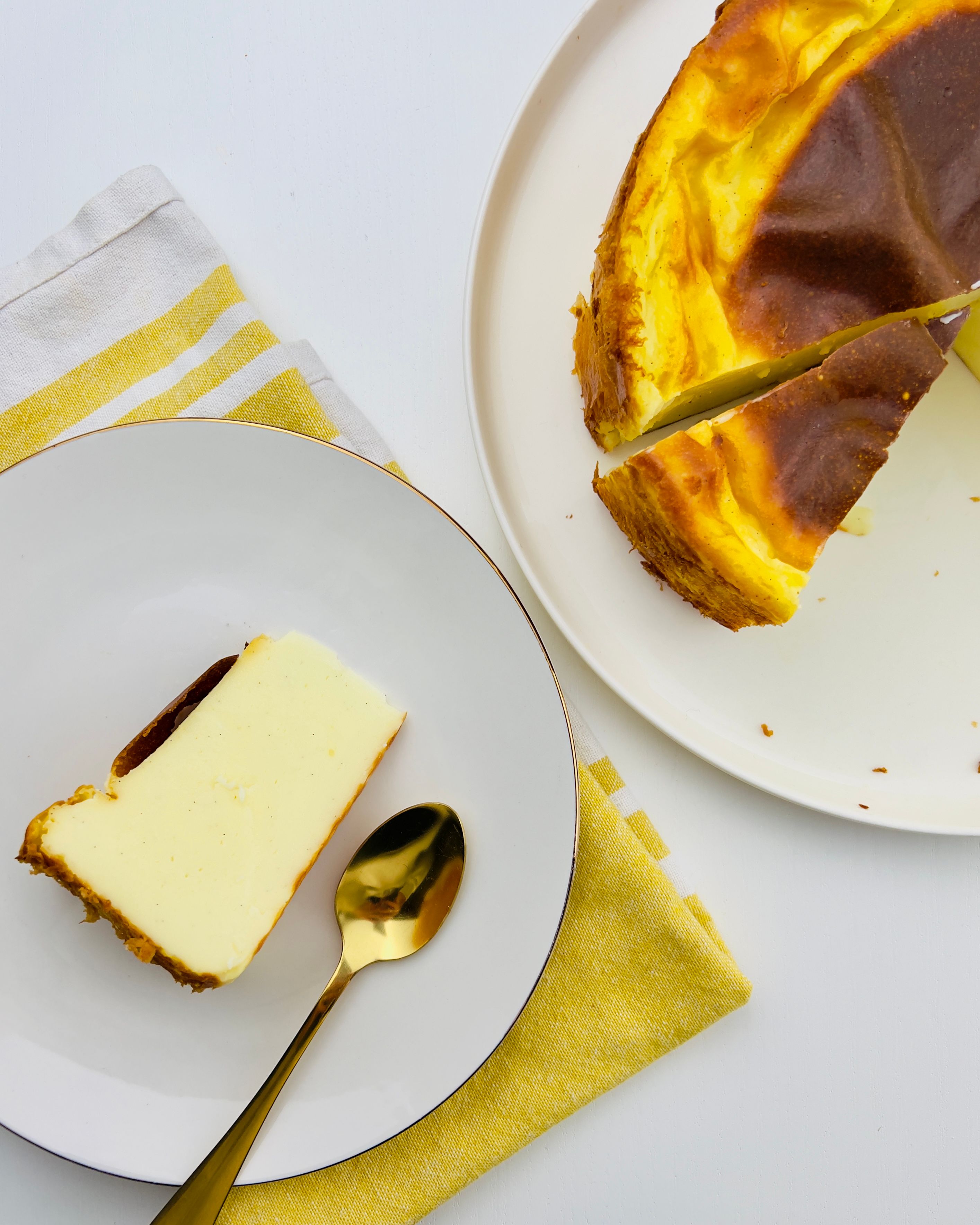 Overhead view of a Basque cheesecake. The whole cheesecake is on a white plate on the right, with a slice on a smaller plate on the left.