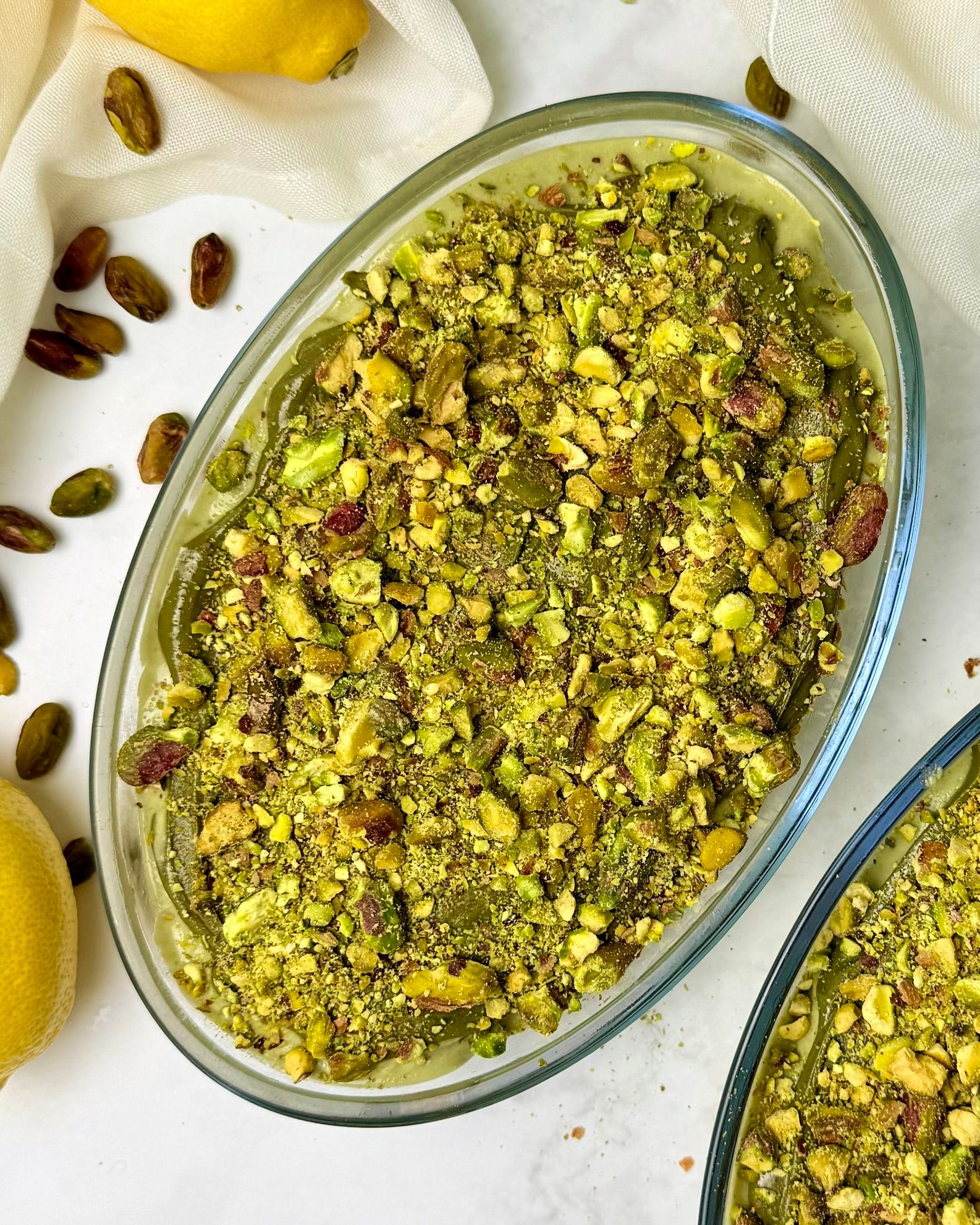 Bright lemon pistachio tiramisu in a clear glass, layered with green pistachio cream and yellow lemon.