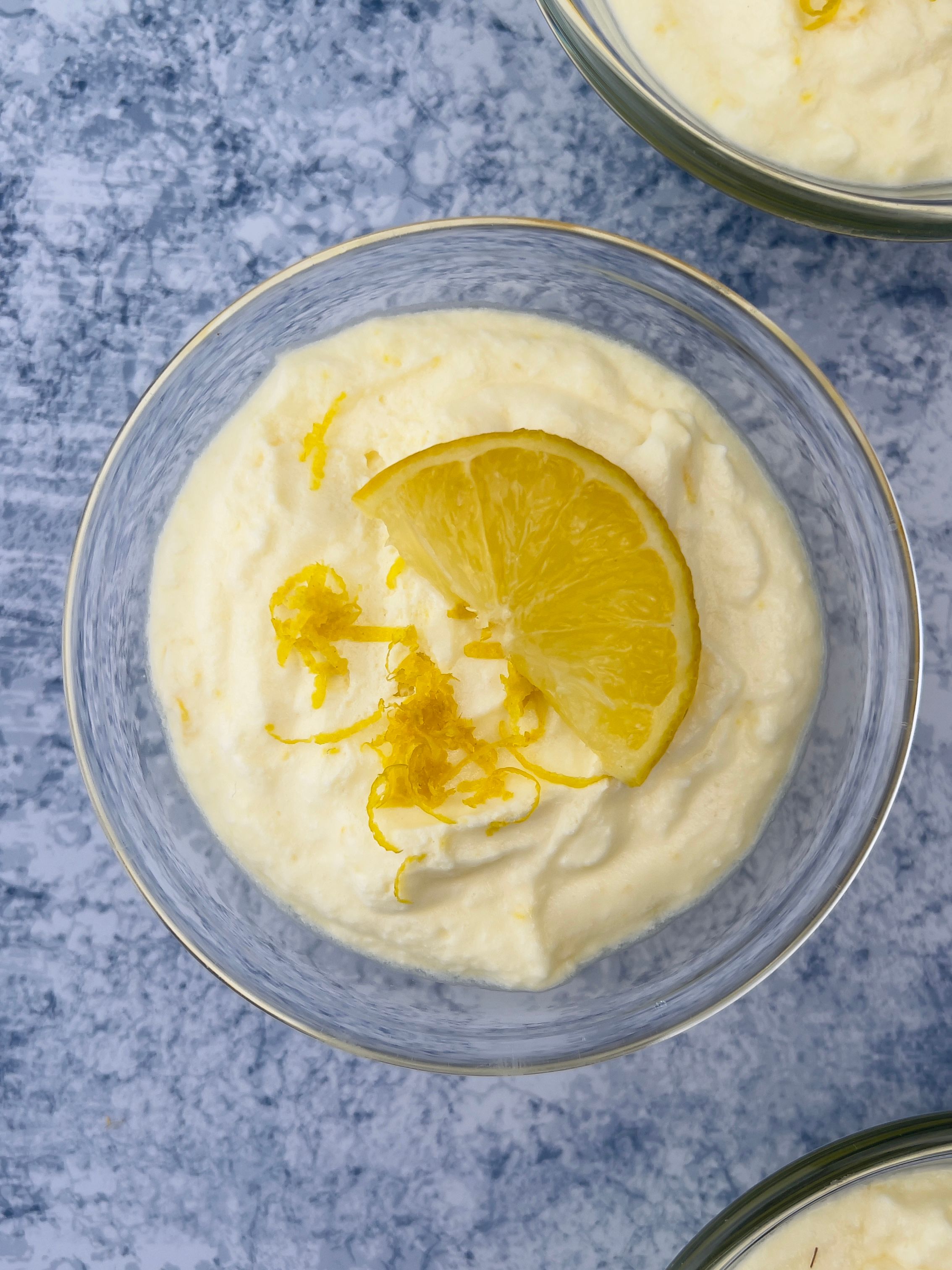 Close-up overhead shot of a single glass filled with a creamy dessert, garnished with lemon zest and a lemon wedge.