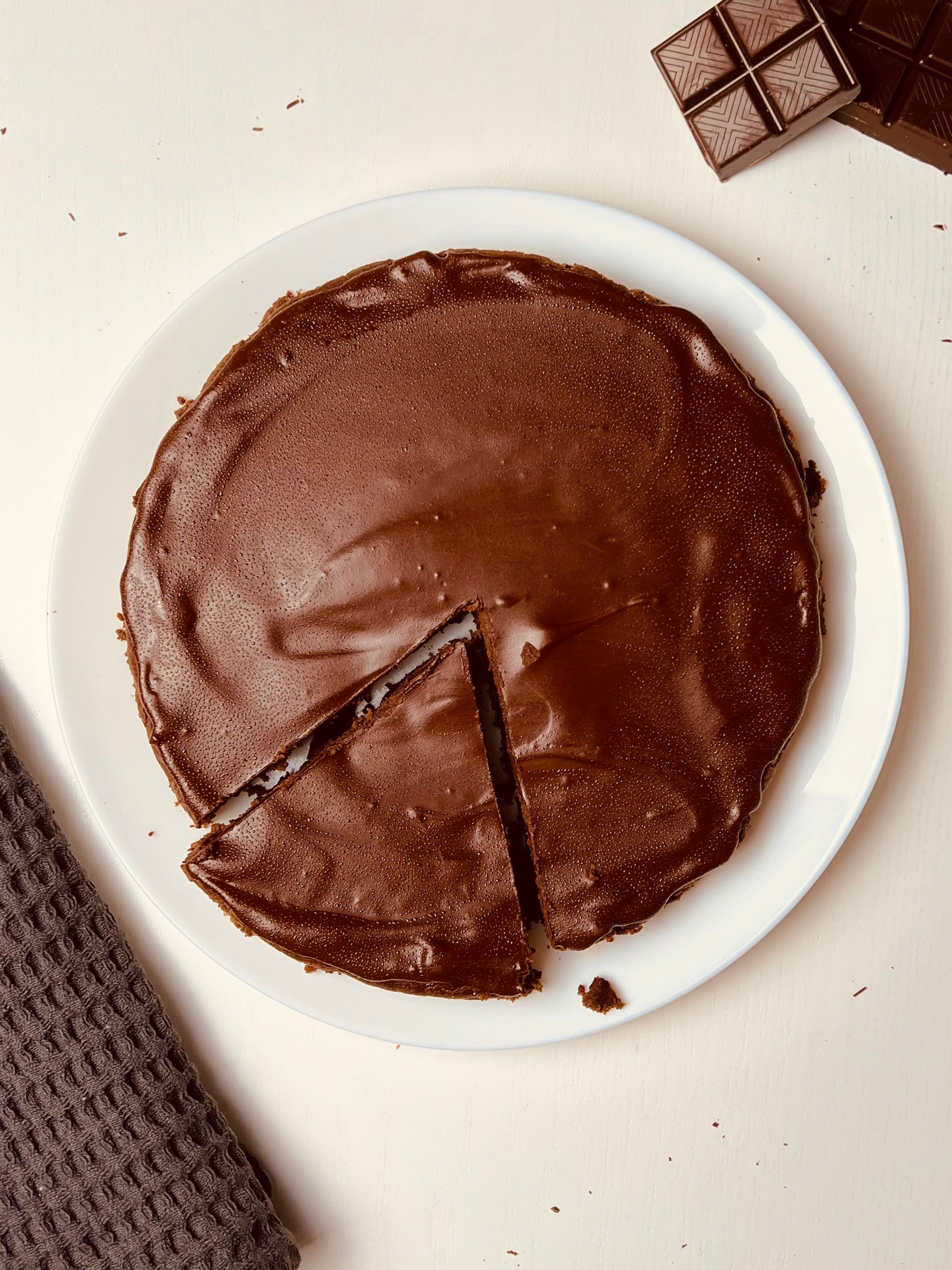 Overhead view of a round brownie on a white plate, with a rich and glossy dark brown top. A portion has been cut from the center showing the fudgy interior.