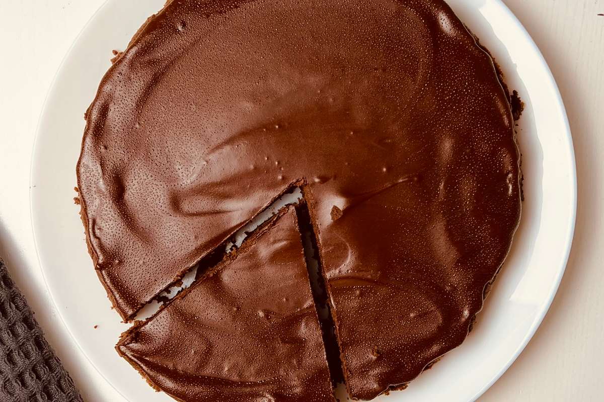 Overhead view of a round brownie on a white plate, with a rich and glossy dark brown top. A portion has been cut from the center showing the fudgy interior.