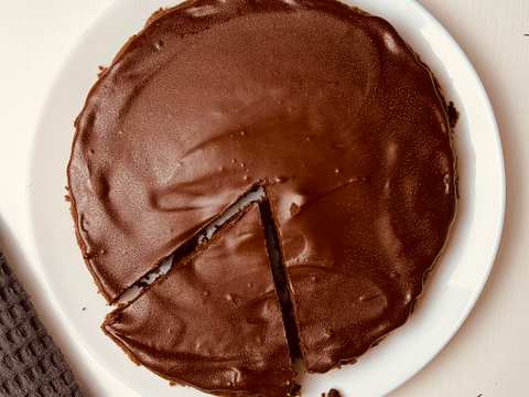 Overhead view of a round brownie on a white plate, with a rich and glossy dark brown top. A portion has been cut from the center showing the fudgy interior.