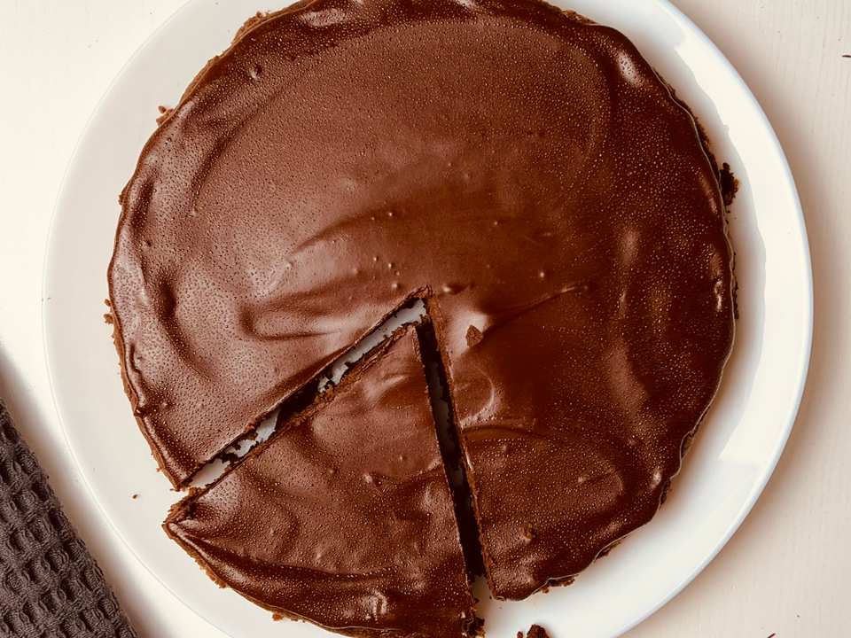 Vue de dessus d'un brownie rond sur une assiette blanche, avec un dessus brun foncé riche et brillant. Une portion a été coupée au centre montrant l'intérieur fondant.