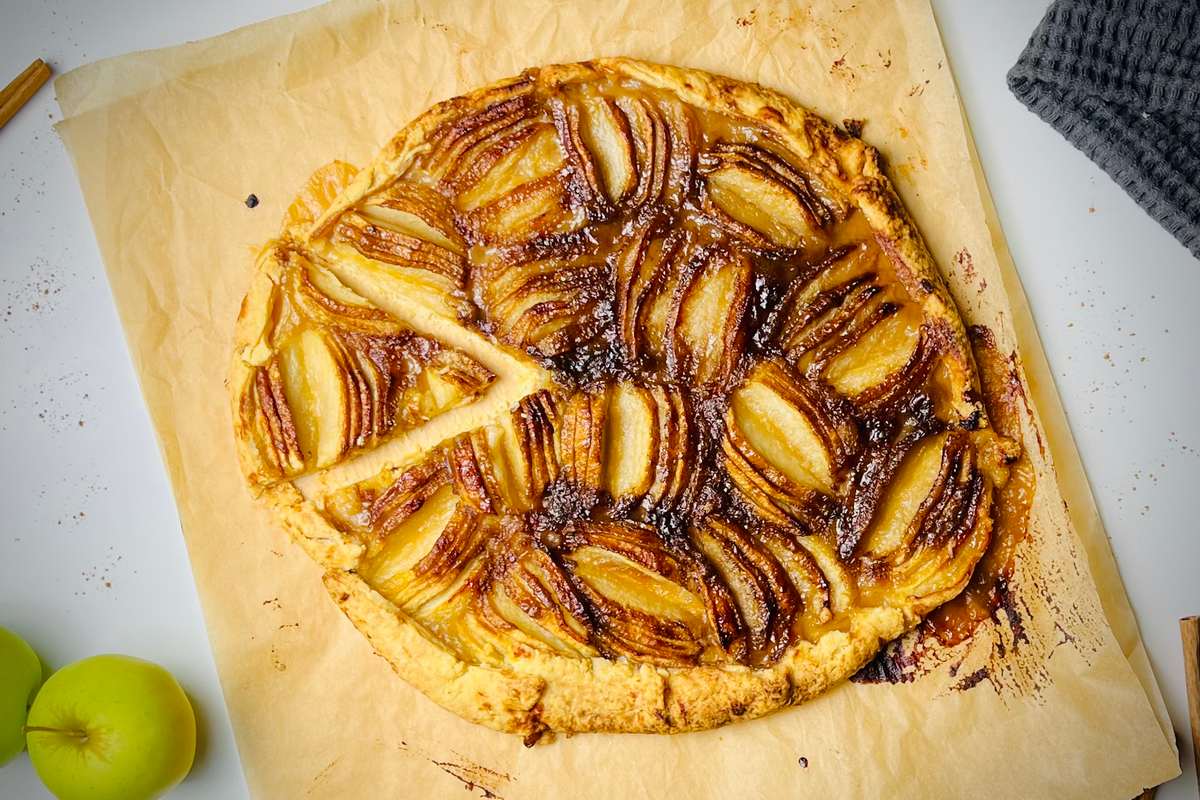 A rustic apple tart with thinly sliced apples arranged in a spiral pattern on a golden crust.