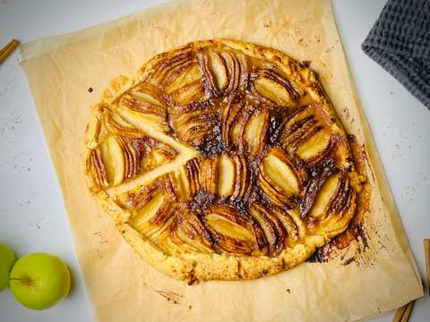 A rustic apple tart with thinly sliced apples arranged in a spiral pattern on a golden crust.