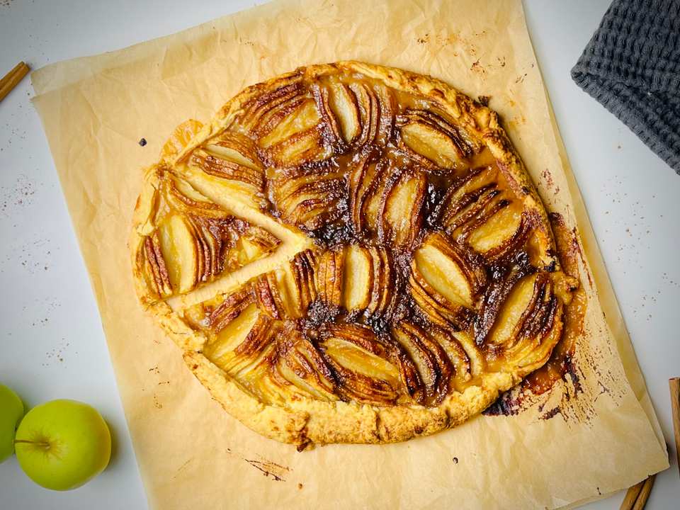 Une tarte rustique aux pommes avec des tranches fines disposées en spirale sur une croûte dorée.