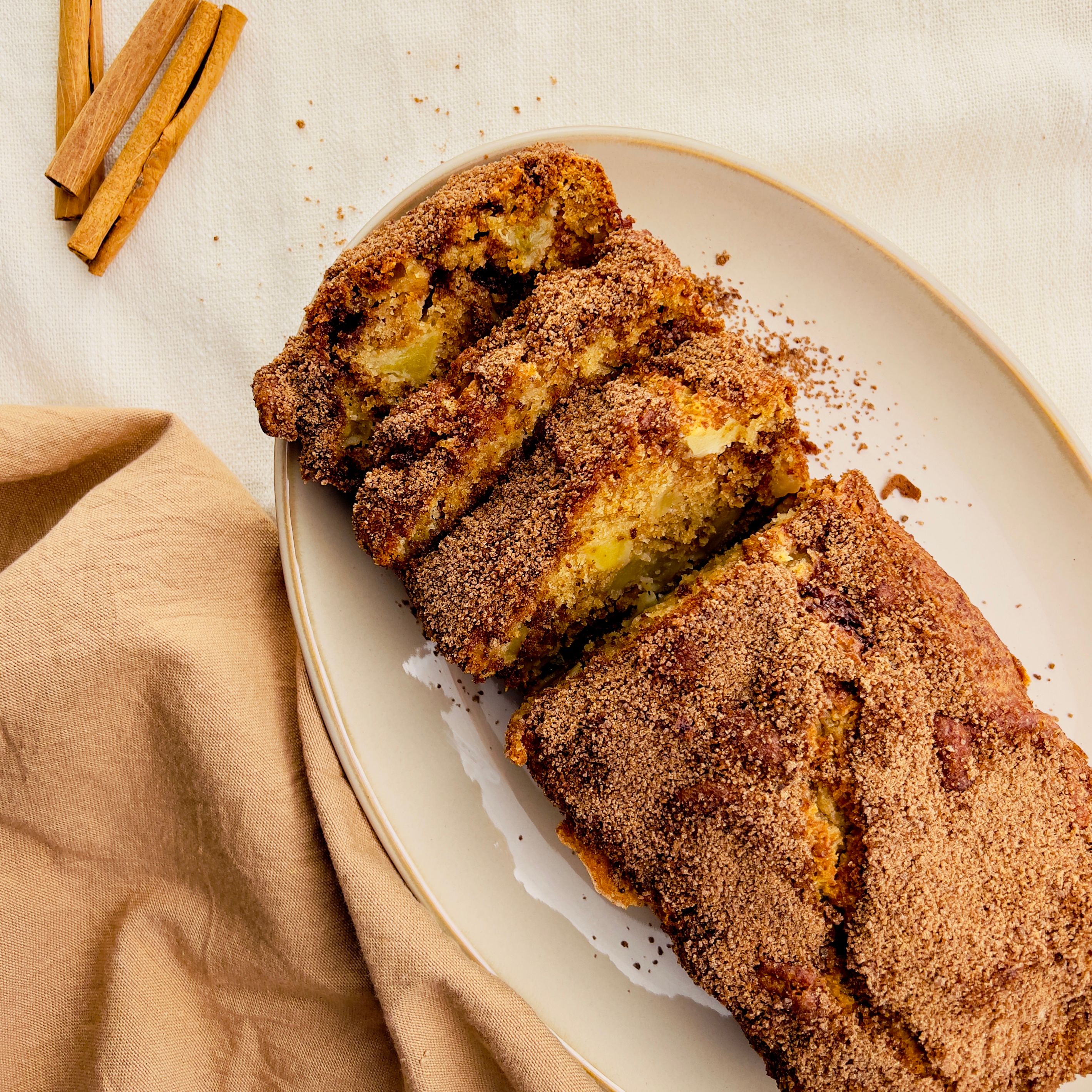Close-up of a pear and chocolate chip loaf cake on a white ceramic plate with a dark green cloth underneath. The sliced loaf reveals a moist interior studded with chocolate chips.