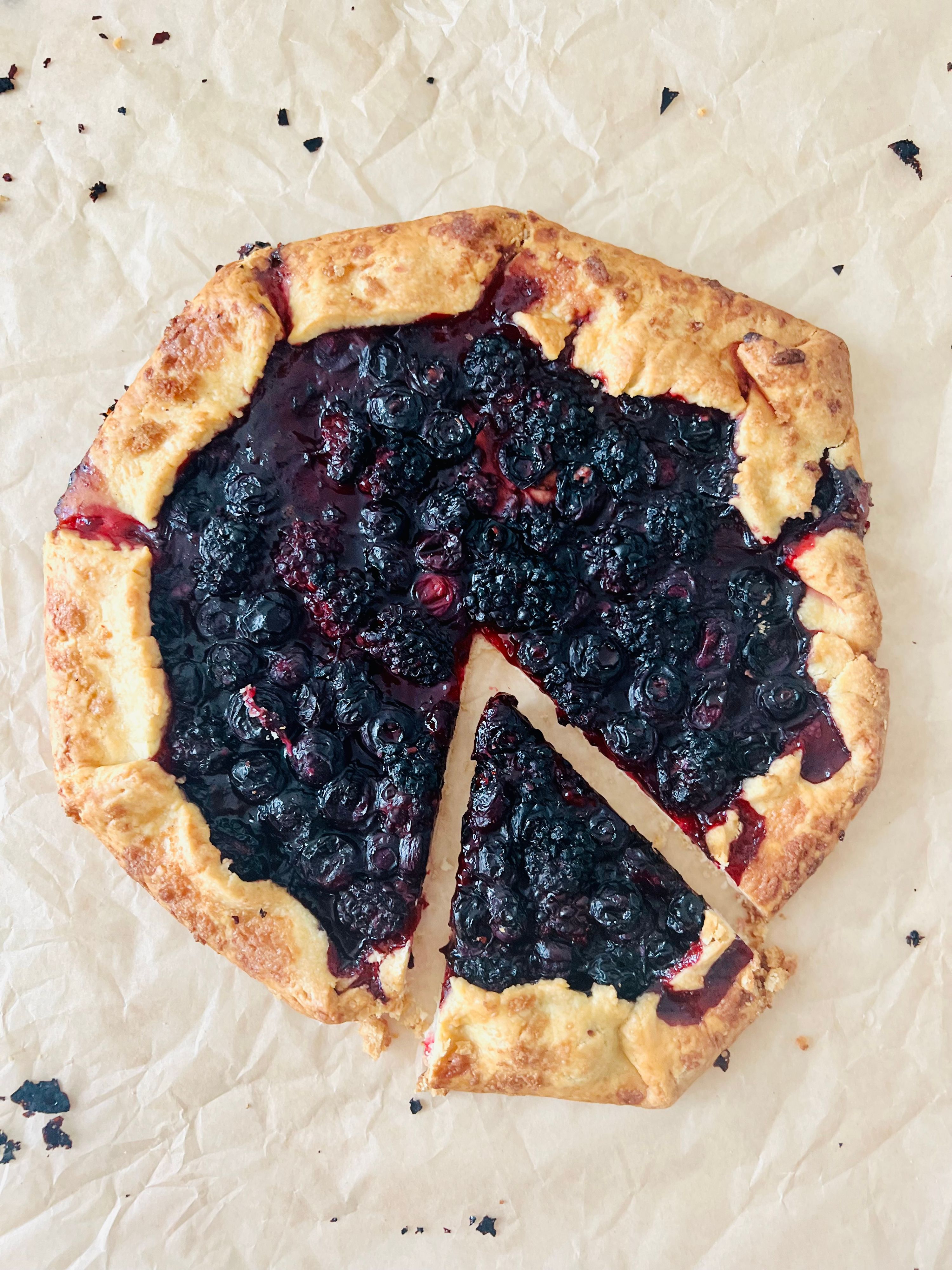 A rustic blueberry and blackberry tart with a golden pastry crust, topped with fresh berries and powdered sugar.