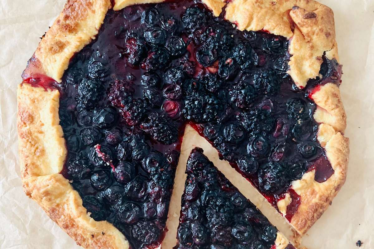 A rustic blueberry and blackberry tart with a golden pastry crust, topped with fresh berries and powdered sugar.