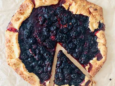 A rustic blueberry and blackberry tart with a golden pastry crust, topped with fresh berries and powdered sugar.