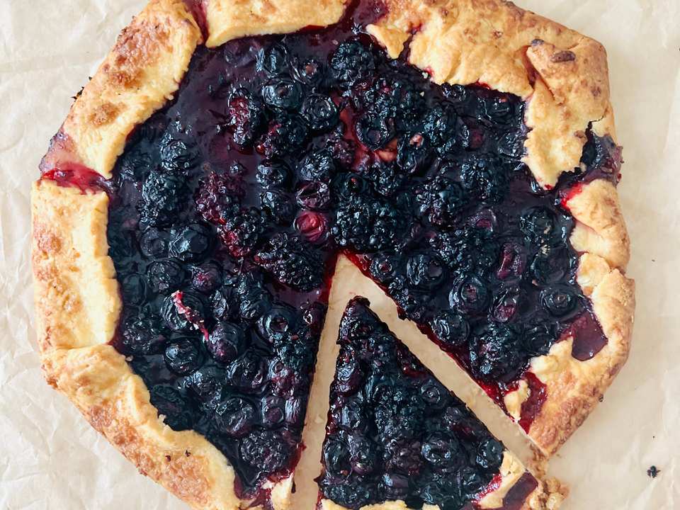 A rustic blueberry and blackberry tart with a golden pastry crust, topped with fresh berries and powdered sugar.
