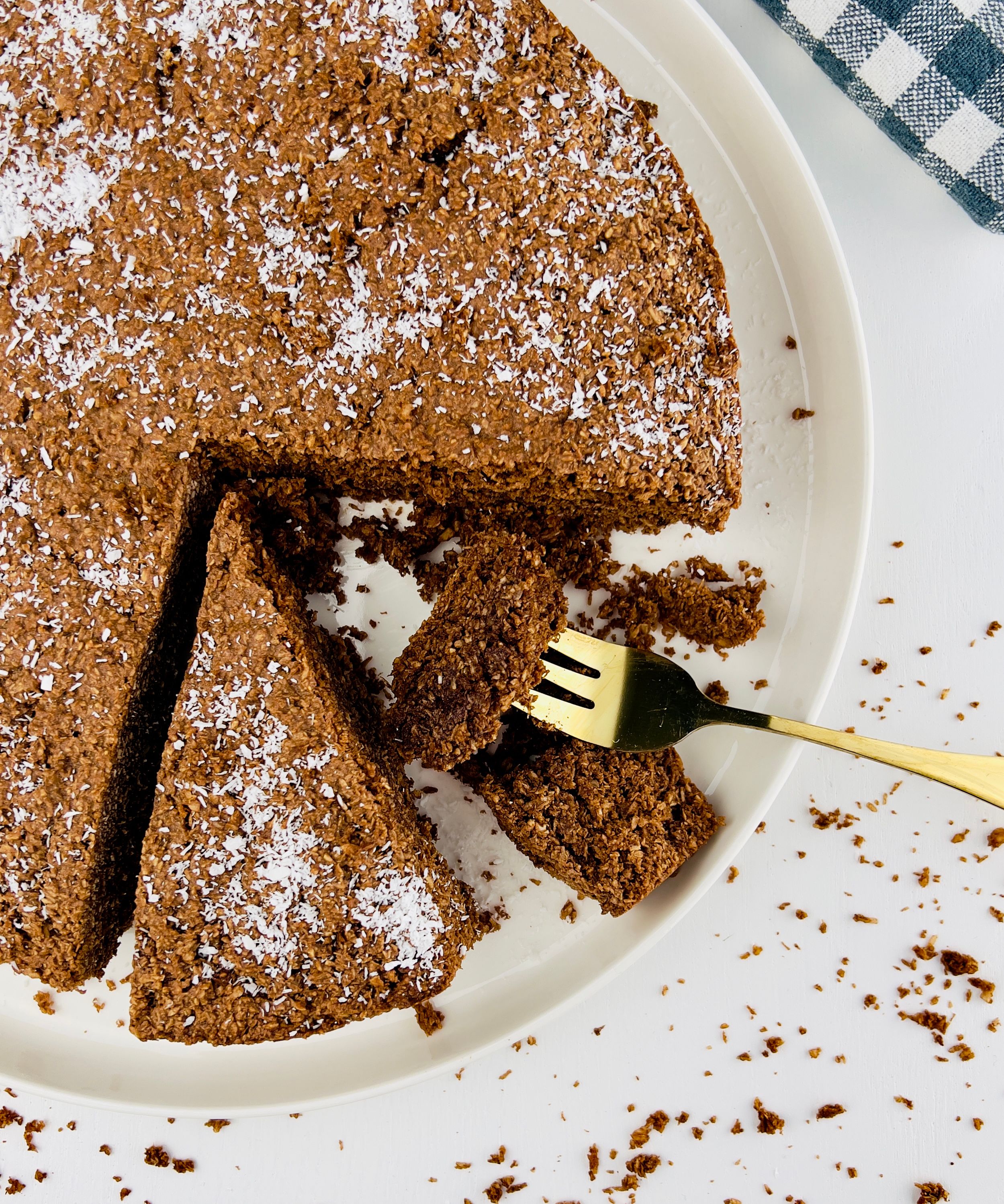 Close up of a homemade round chocolate oatmeal cake, with one slice cut out, sprinkled with shredded coconut.