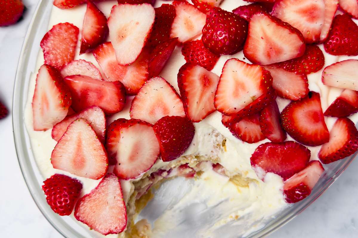 Vue plongeante d'un plat en verre en grande partie rempli d'un dessert de crème blanche et de fraises rouges tranchées; une portion a été servie.