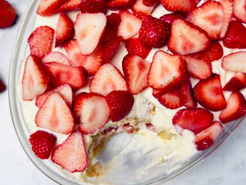 Overhead view of a glass dish mostly filled with a dessert of white cream and red sliced strawberries; a serving has been scooped out.
