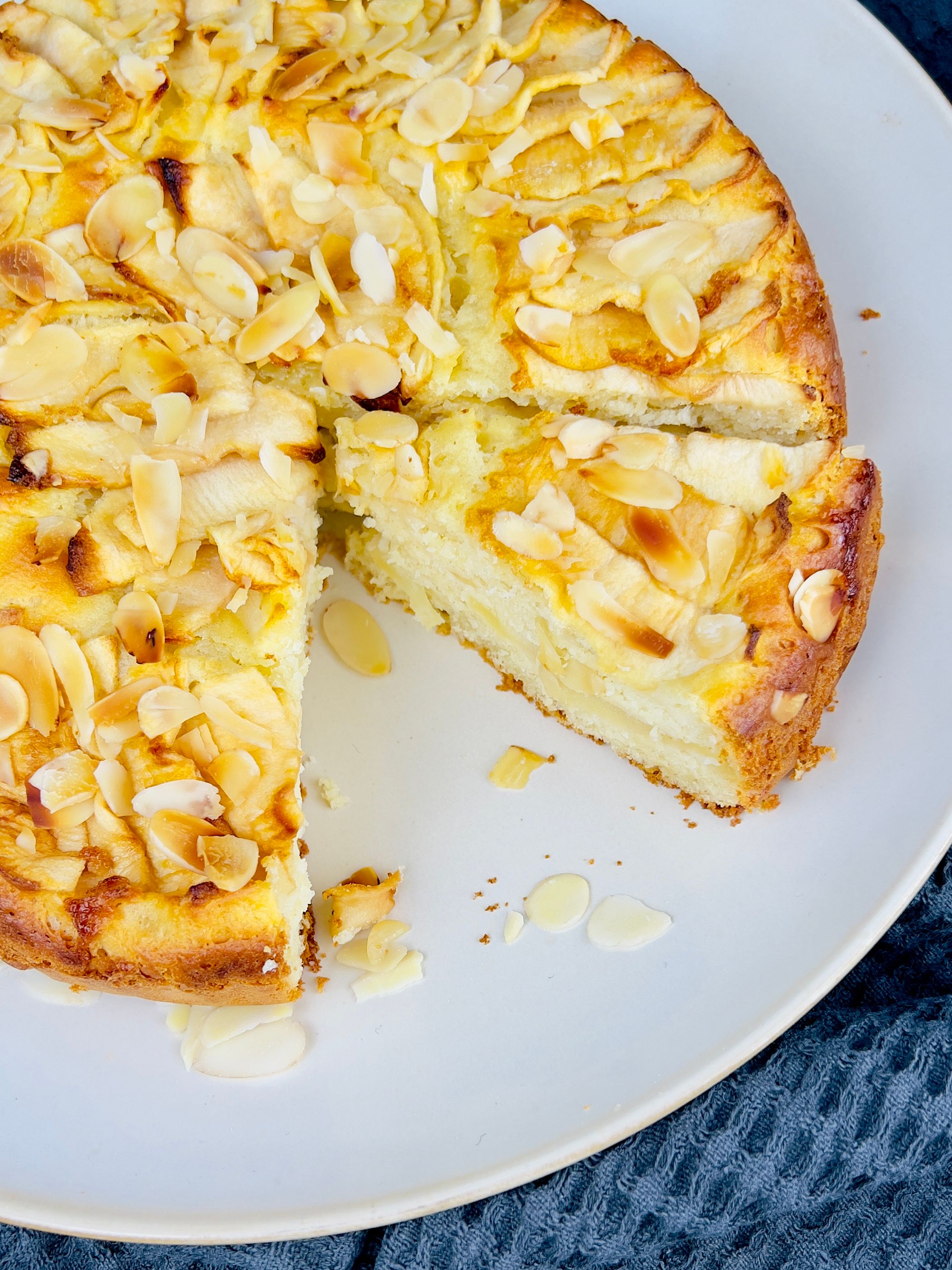 A fluffy, golden apple and coconut cake, dusted with coconut flakes, on a wire rack.