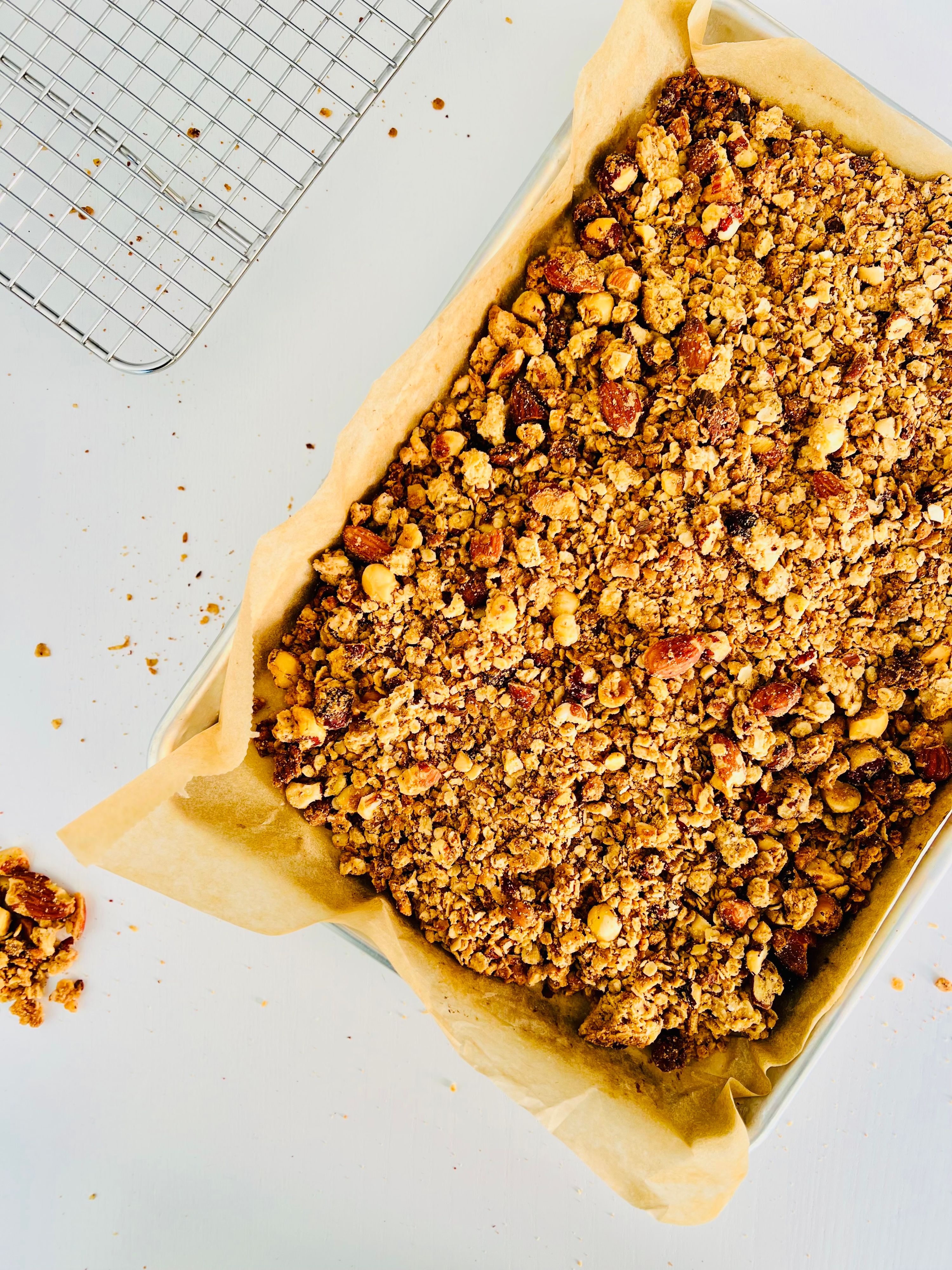 Overhead close-up of crunchy granola clusters with visible peanuts and oats spread on a baking sheet.