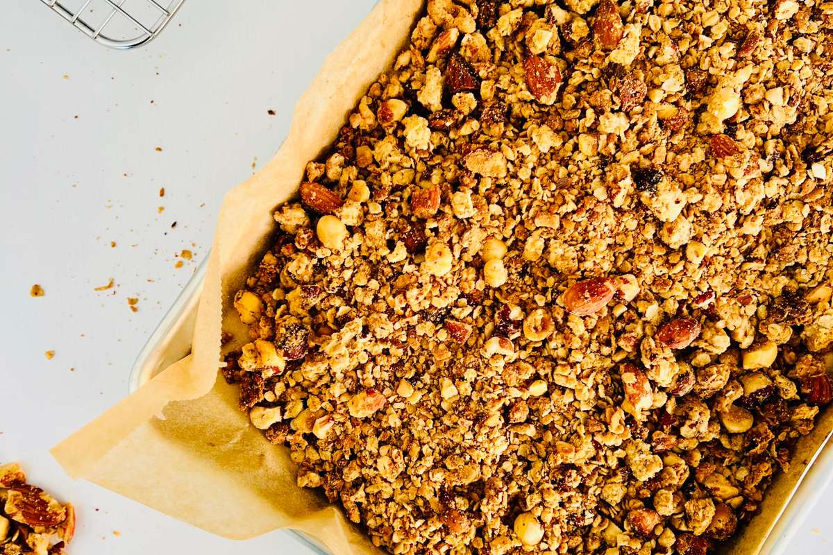 Overhead close-up of crunchy granola clusters with visible peanuts and oats spread on a baking sheet.