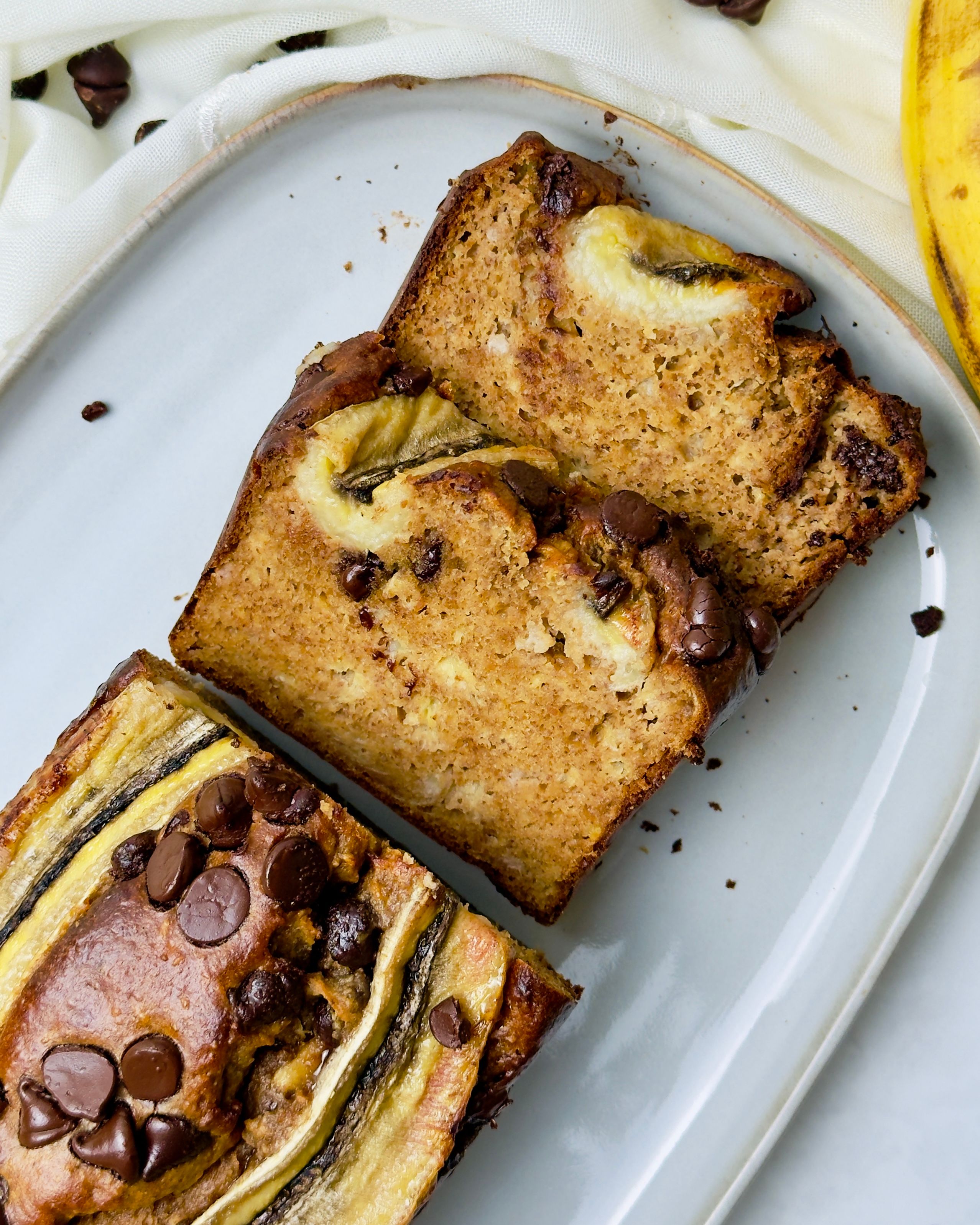 Three slices of banana bread with chocolate chips and banana pieces on top are arranged on a white rectangular plate.