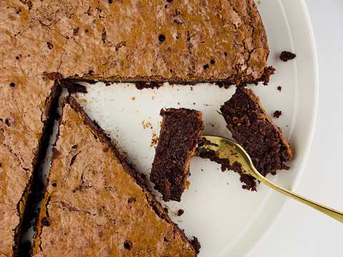A round, dark chocolate cake with a cracked top and visible hazelnuts, dusted lightly, on a cooling rack.