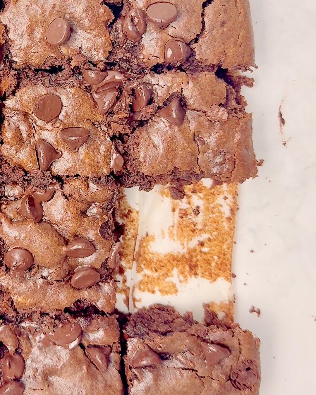 Close up overhead shot of a pan of cut brownies, one missing slice revealing the pan bottom covered in parchment paper.