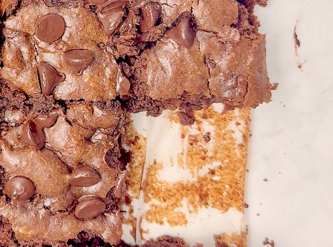Close up overhead shot of a pan of cut brownies, one missing slice revealing the pan bottom covered in parchment paper.
