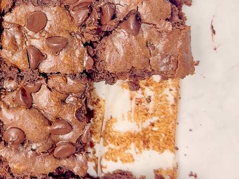 Close up overhead shot of a pan of cut brownies, one missing slice revealing the pan bottom covered in parchment paper.
