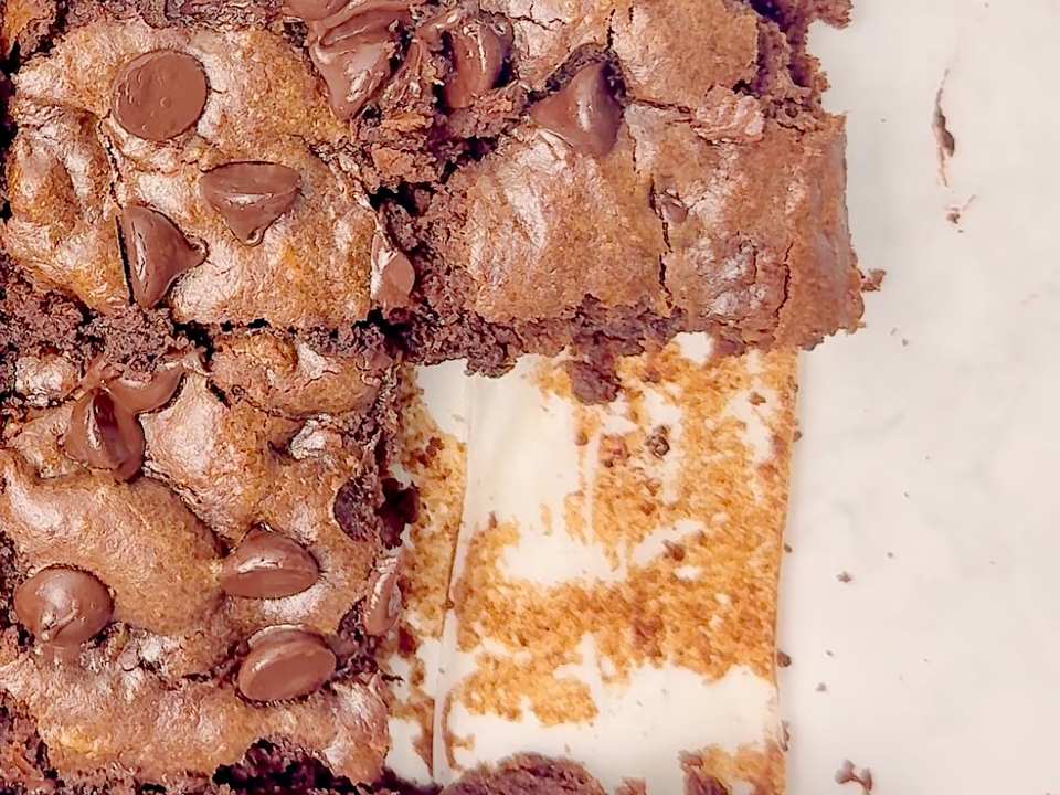 Gros plan en plongée sur un plat de brownies coupés, une tranche manquante révélant le fond du plat tapissé de papier sulfurisé.