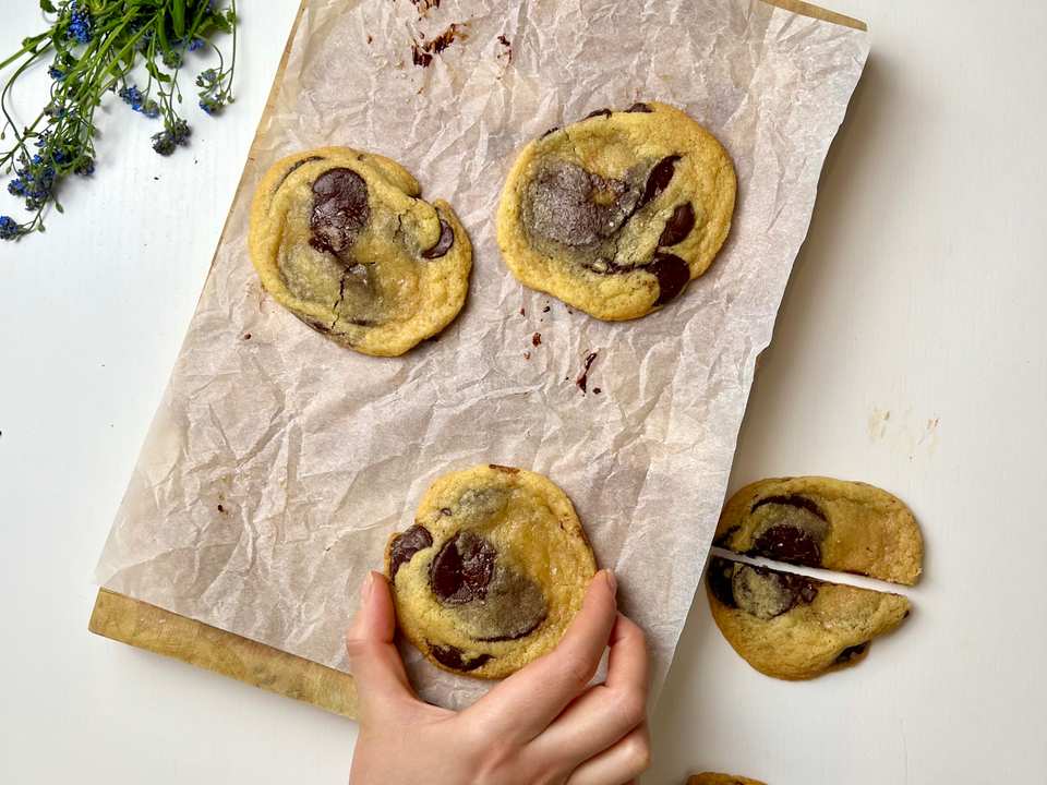 Gros plan d'un cookie aux pépites de chocolat doré avec du sel de mer sur le dessus, posé sur une grille de refroidissement, avec un verre de lait en arrière-plan.