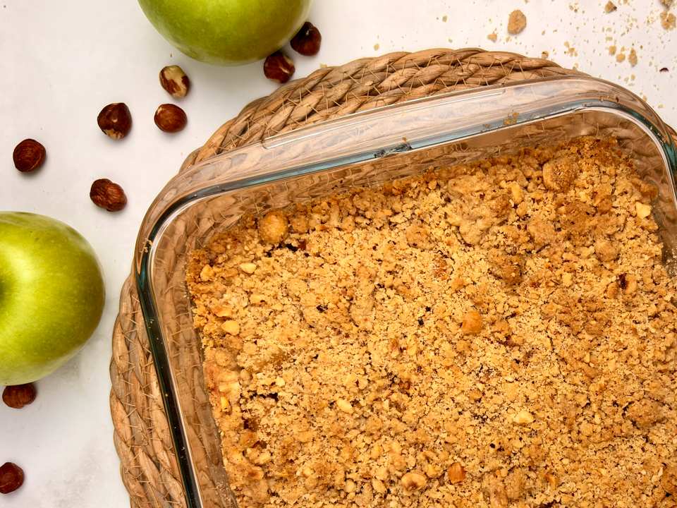 Vue de dessus d'un riche gâteau au chocolat, garni de fruits à coque hachés mélangés, sur une assiette en céramique claire, avec une part coupée.