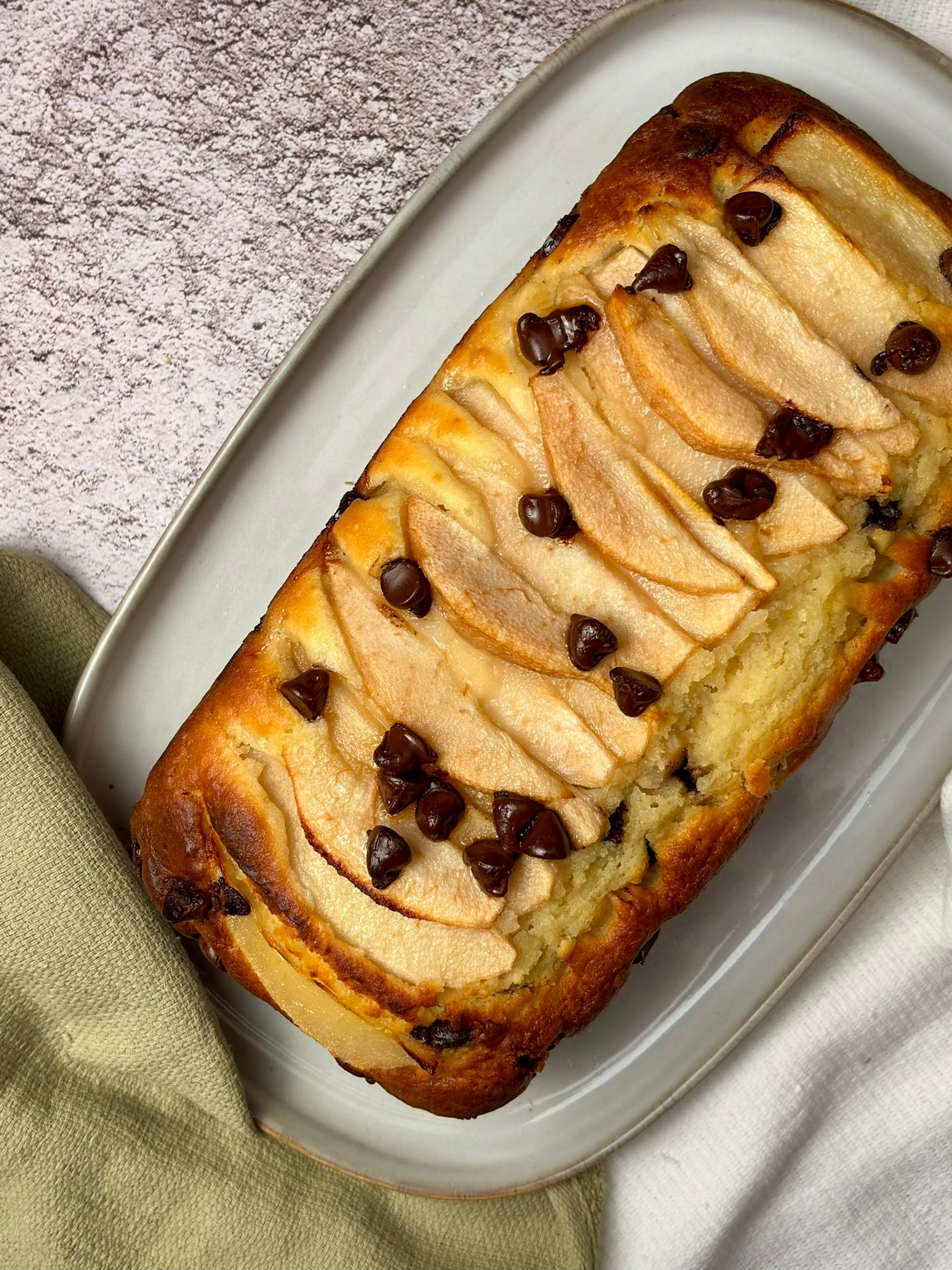 Two clear bowls of yogurt topped with caramelized banana slices. A spoon with cinnamon is between the bowls, on a white countertop.