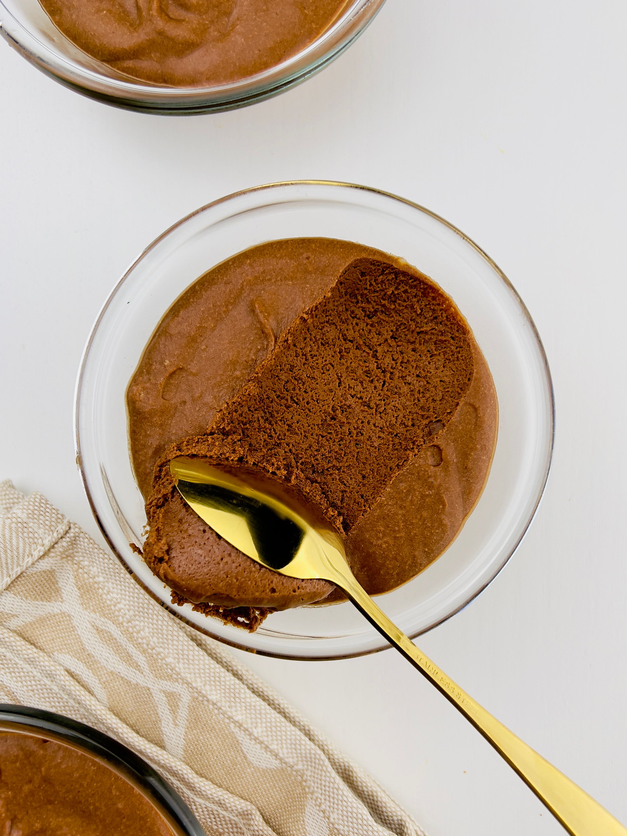 Overhead shot of a rich chocolate mousse in a clear glass bowl, with a gold spoon scooping out a portion, showing its fluffy texture.